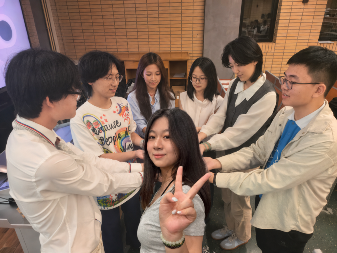 七名助理部成员围成一圈叠手合影，前排同学面向镜头比出胜利手势